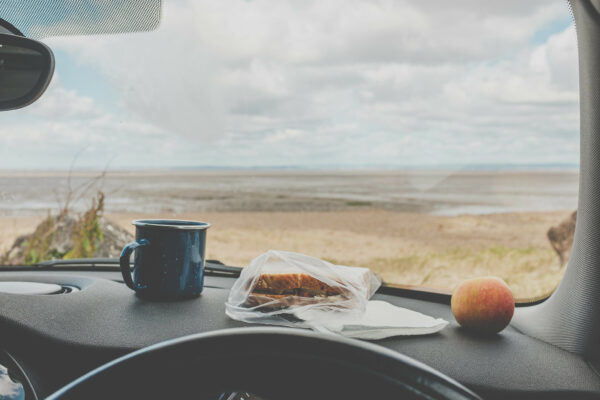 Cheese and pickle sandwich, apple and pannikin of tea on a car dashboard